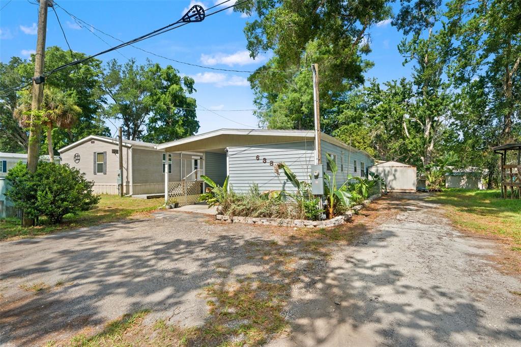 A single-story mobile home with a carport and a gravel driveway under large trees — 6380 RICHARD DRIVE, WEEKI WACHEE, FL
