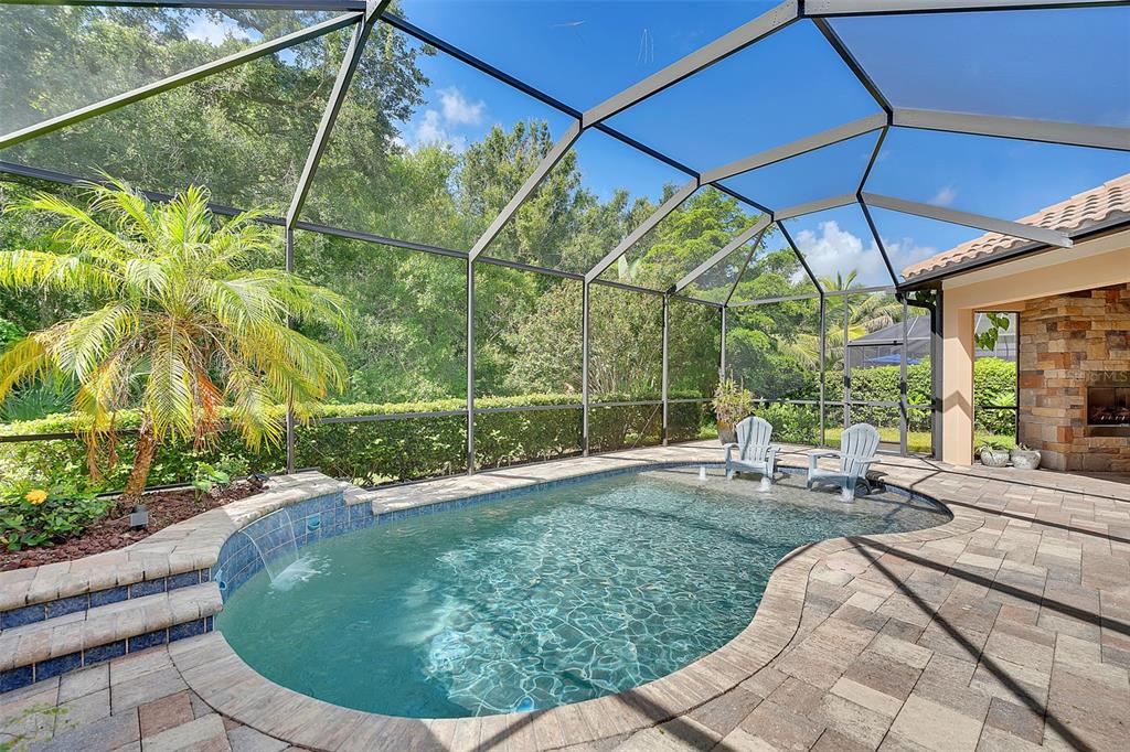 A screened-in patio features a swimming pool with a water feature and stone pavers — 10310 EASTWOOD DRIVE, BRADENTON, FL