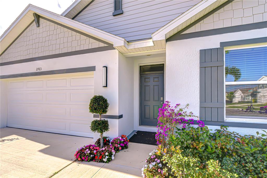 A front view of a house exterior featuring a garage, a gray door, and landscaping — 2763 WIDEWATER WAY, ZEPHYRHILLS, FL