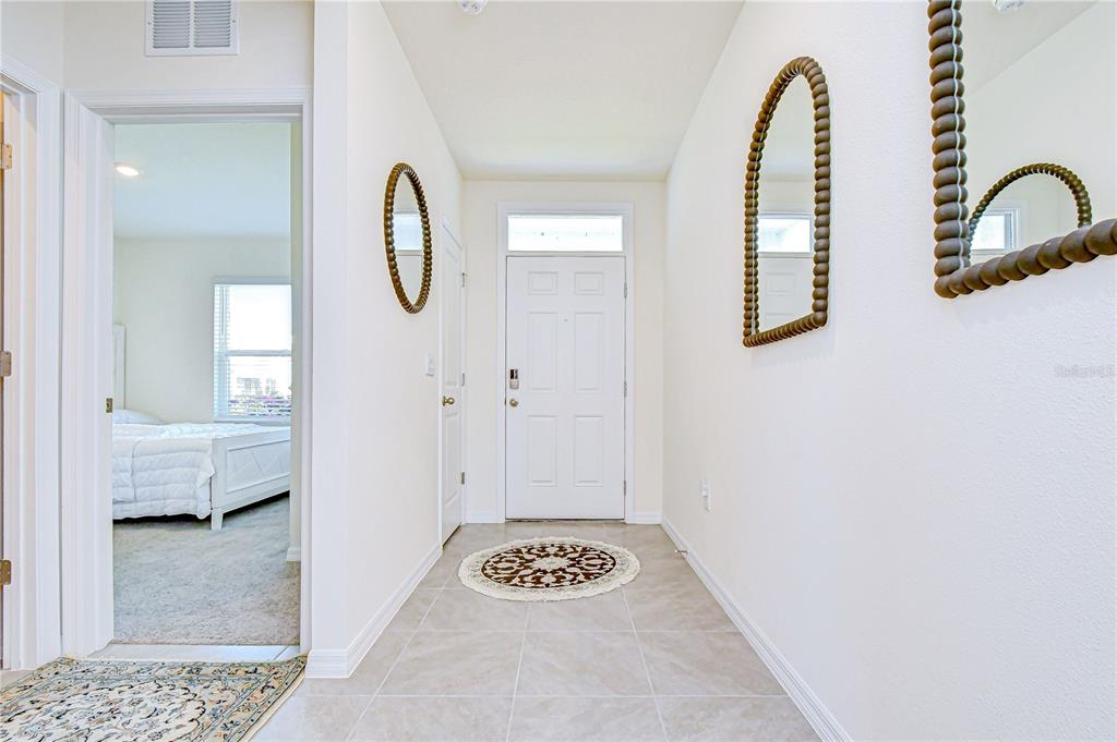 A tiled entryway features a white front door, two wall mirrors, and an adjacent bedroom — 2763 WIDEWATER WAY, ZEPHYRHILLS, FL