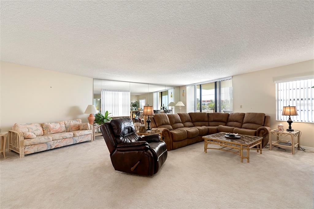 A living room features a large brown sectional, a patterned sofa, and a mirrored wall — 6500 SUNSET WAY UNIT 116, ST PETE BEACH, FL