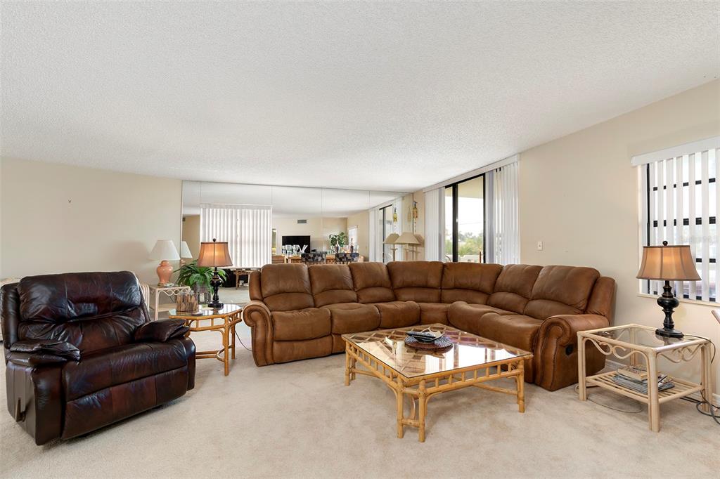 A living room features a brown sectional sofa, a leather recliner, and glass-topped bamboo tables — 6500 SUNSET WAY UNIT 116, ST PETE BEACH, FL