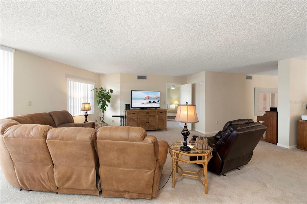 A living room features a tan sectional sofa, a brown recliner, and a television console — 6500 SUNSET WAY UNIT 116, ST PETE BEACH, FL