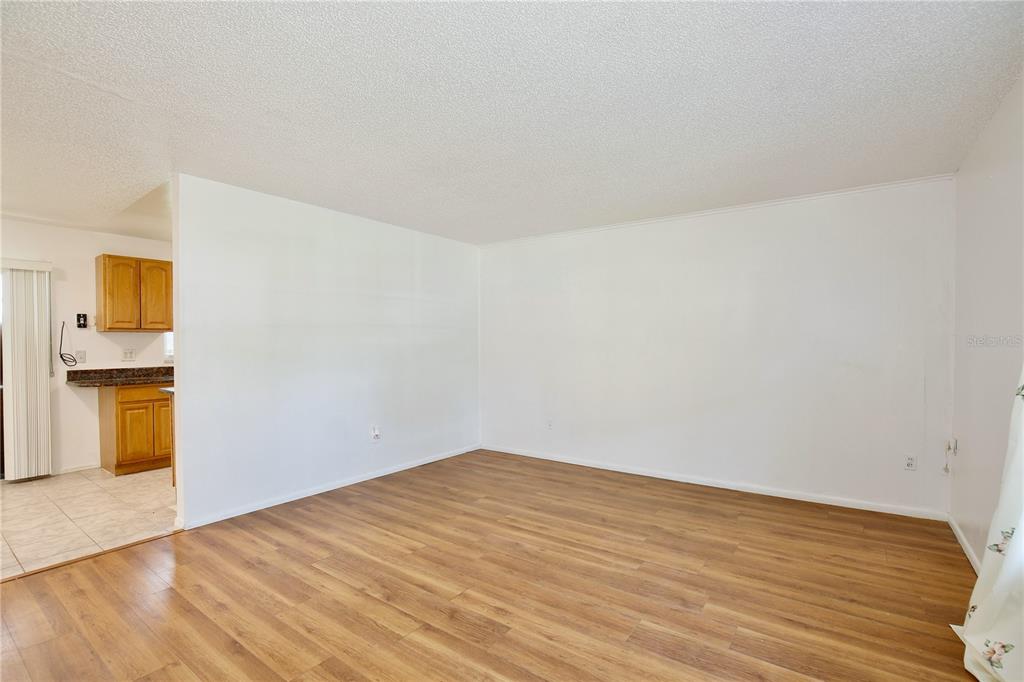 An empty living room with light wood-look flooring and white walls opens to a kitchen — 2319 CONTINENTAL BOULEVARD, ORLANDO, FL