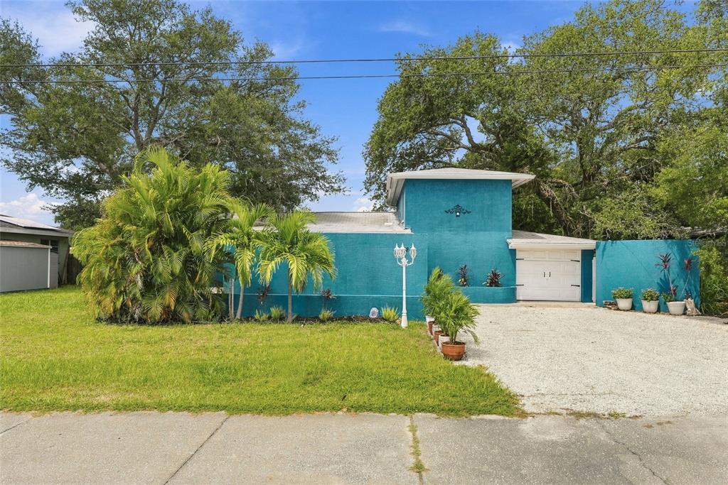 A blue exterior wall, a white garage door, and a gravel driveway are shown — 4720 WELCH CAUSEWAY, ST PETERSBURG, FL