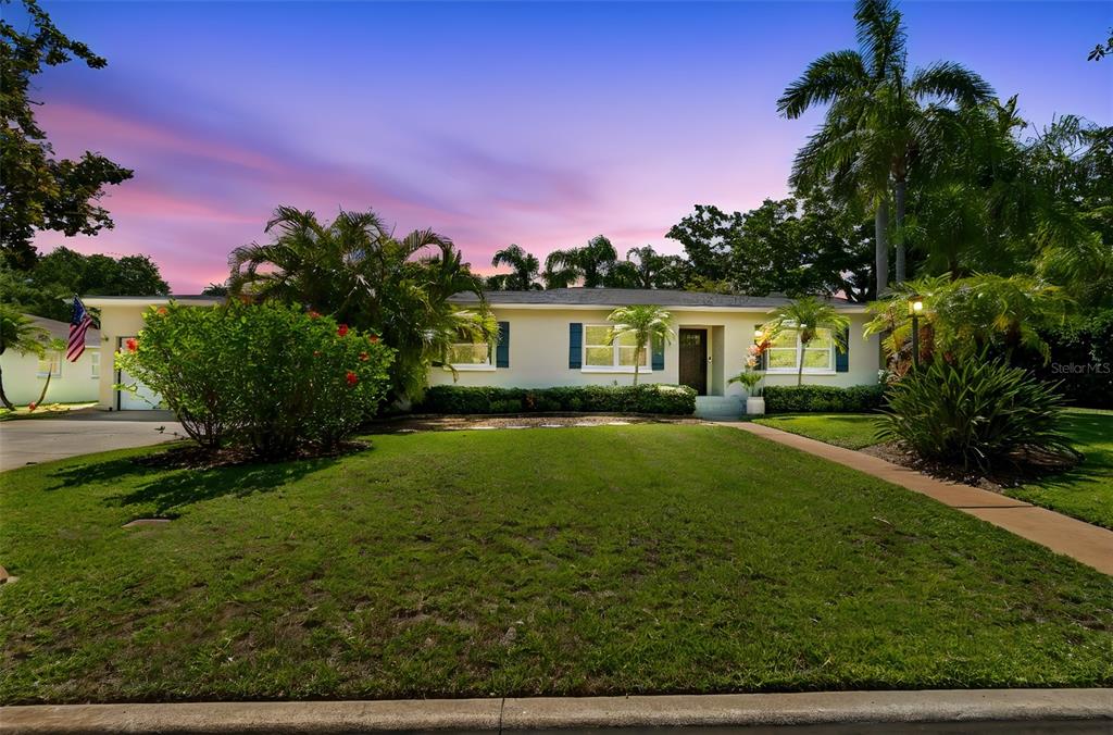 A wooden front door with sidelights sits on a porch with potted flowers and a mat — 1743 EAGLES NEST DRIVE, BELLEAIR, FL