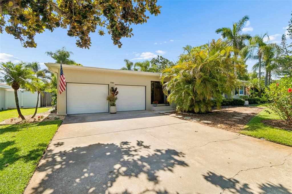 A front entrance with a dark wood door, a welcome mat, and potted red flowers — 1743 EAGLES NEST DRIVE, BELLEAIR, FL