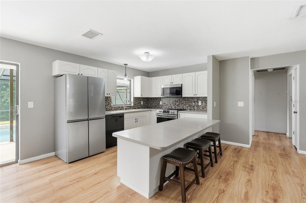 A kitchen with white cabinets, stainless steel appliances, a center island, and wood-look flooring — 28265 MORNINGSIDE DRIVE, PUNTA GORDA, FL