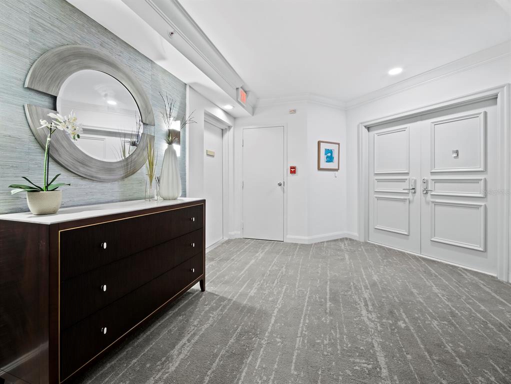 A hallway features a dark wood dresser, a circular mirror, and double doors on carpeted flooring — 565 SANCTUARY DRIVE UNIT B106, LONGBOAT KEY, FL