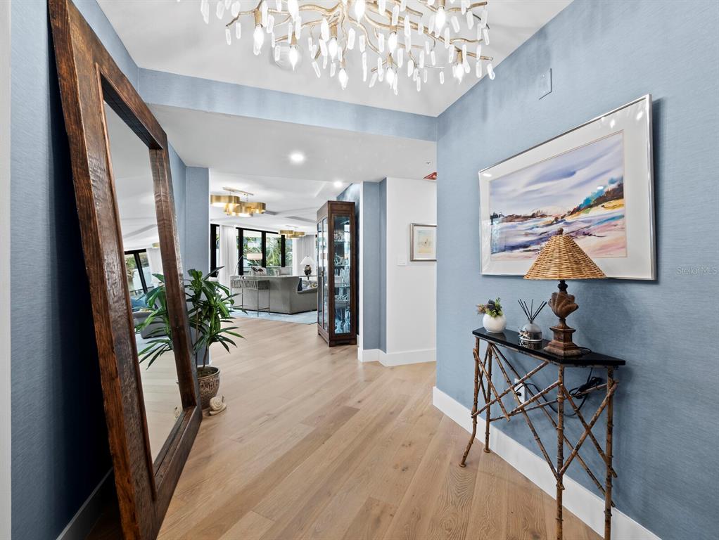 A foyer with light wood floors, blue walls, a large floor mirror, and a crystal chandelier — 565 SANCTUARY DRIVE UNIT B106, LONGBOAT KEY, FL