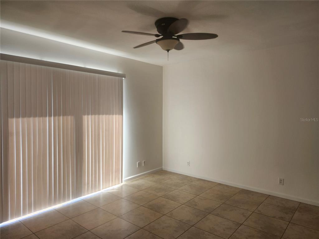 An empty room features light-colored tile flooring, white walls, a ceiling fan, and vertical blinds — 14656 WAKE ROBIN DRIVE, BROOKSVILLE, FL