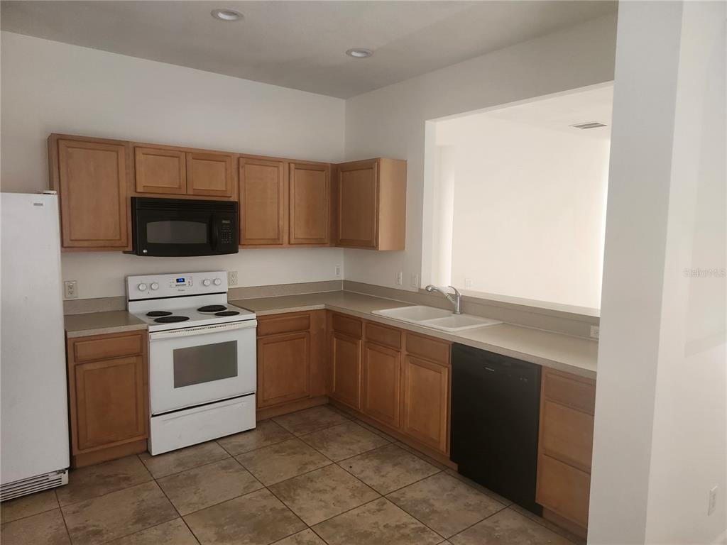 A kitchen features light wood cabinets, white appliances, a double sink, and tiled flooring — 14656 WAKE ROBIN DRIVE, BROOKSVILLE, FL