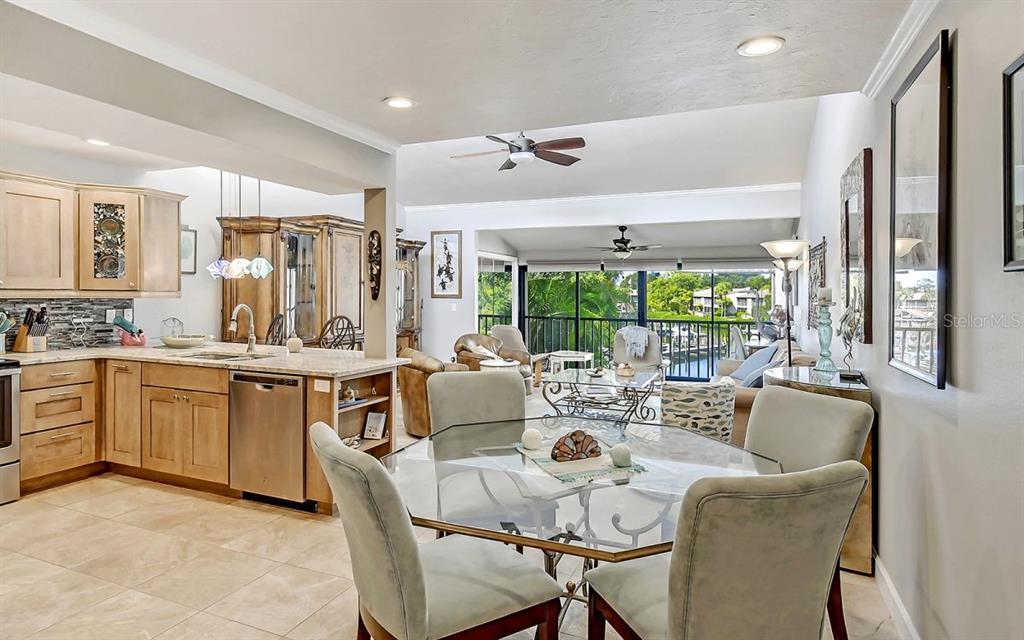 An open-concept kitchen and dining area features light wood cabinets, tile flooring, and a balcony view — 1633 BOATHOUSE CIRCLE UNIT HA233, SARASOTA, FL