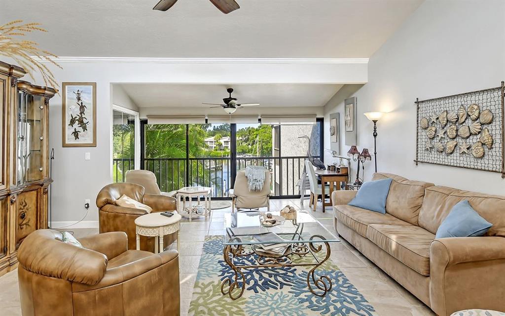 A living room features tan leather furniture, a glass coffee table, and a balcony view — 1633 BOATHOUSE CIRCLE UNIT HA233, SARASOTA, FL