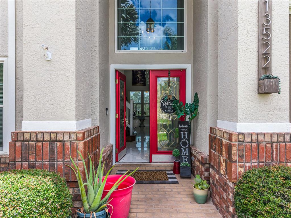The front entrance of a house features a red double door, brick accents, and landscaping — 13522 HERON CAY COURT, ORLANDO, FL