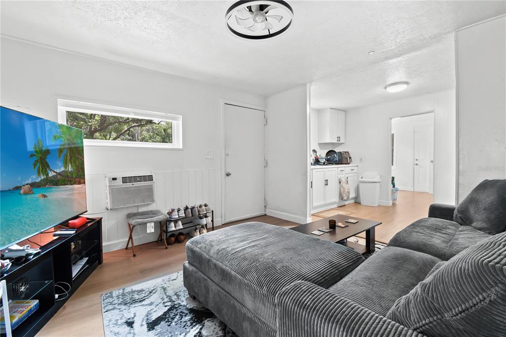 A living room features a grey sectional sofa, a television, and an adjacent kitchen area — 725 NEW YORK ST, CLEARWATER, FL