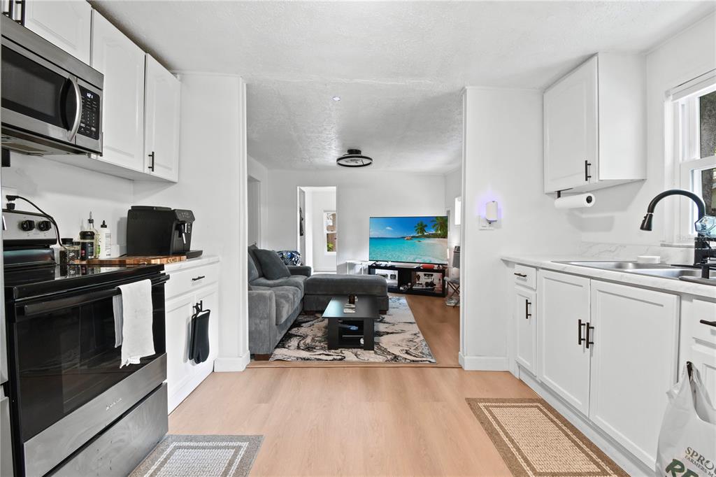 A white kitchen with stainless steel appliances opens into a living room with a sofa — 725 NEW YORK ST, CLEARWATER, FL