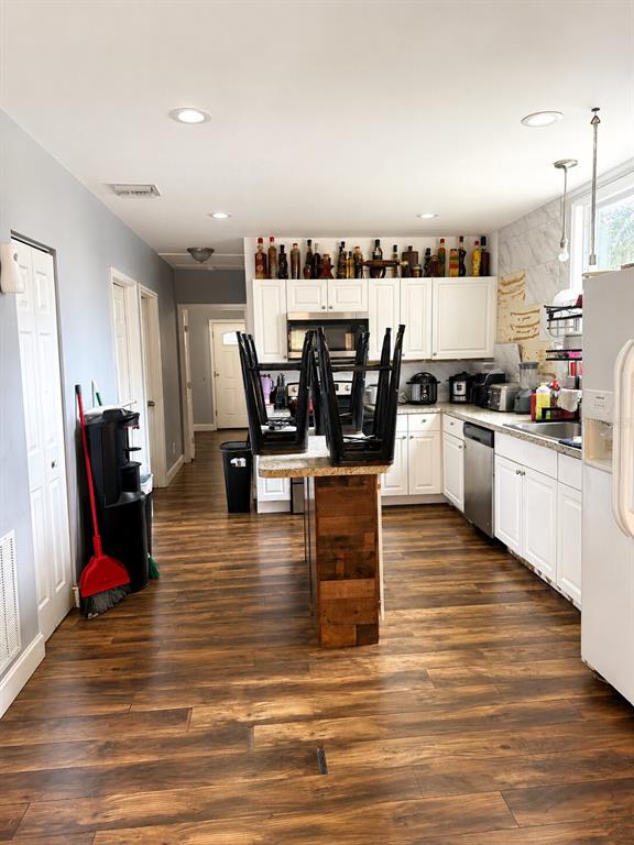 A kitchen features white cabinets, a wood-paneled island with stools, and dark wood-look flooring — 1604 ANGLE ROAD, FORT PIERCE, FL
