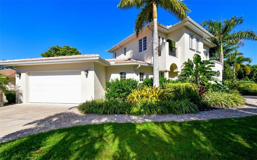 A two-story house with a white garage, beige stucco exterior, and lush tropical landscaping — 1179 MORNINGSIDE PLACE, SARASOTA, FL