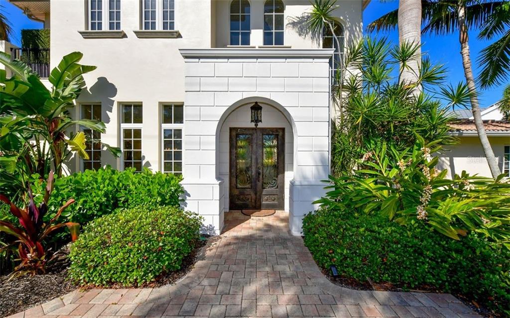 A paved walkway leads to the arched entryway of a white house with double doors — 1179 MORNINGSIDE PLACE, SARASOTA, FL