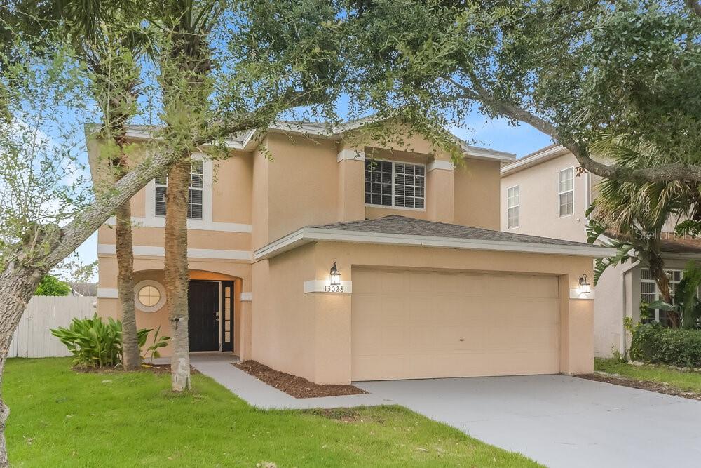 A two-story tan stucco house features a two-car garage and a front entrance walkway — 13028 LILY POND COURT, ORLANDO, FL