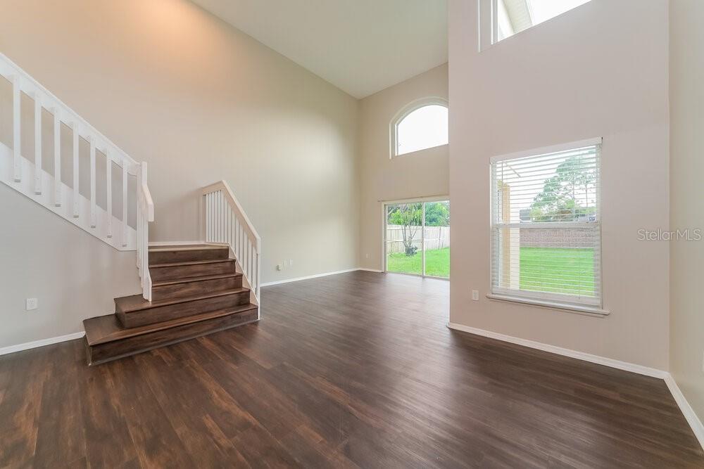 A living room with dark wood flooring, a staircase, and a large window overlooking grass — 13028 LILY POND COURT, ORLANDO, FL