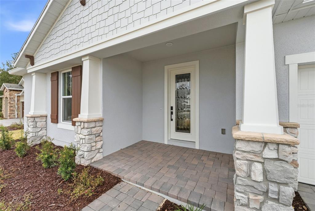 A covered front porch features stone-based columns, a glass-paneled door, and brown shutter accents — 3500 LEMON BUTTON TERRACE, APOPKA, FL