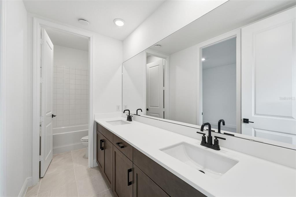 A bathroom features a double vanity with dark wood cabinets, white countertops, and black fixtures — 3500 LEMON BUTTON TERRACE, APOPKA, FL
