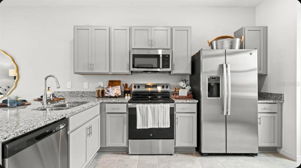A kitchen features gray cabinets, stainless steel appliances, and speckled granite countertops — 671 NESS ISLAND DRIVE UNIT 0, MOUNT DORA, FL