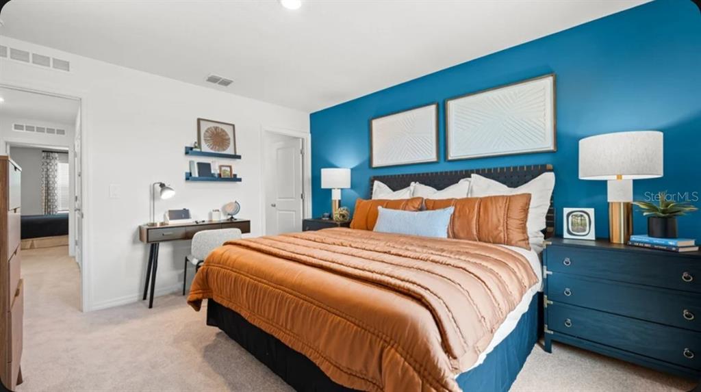 A bedroom features a blue accent wall, a bed with orange bedding, and a small desk — 671 NESS ISLAND DRIVE UNIT 0, MOUNT DORA, FL