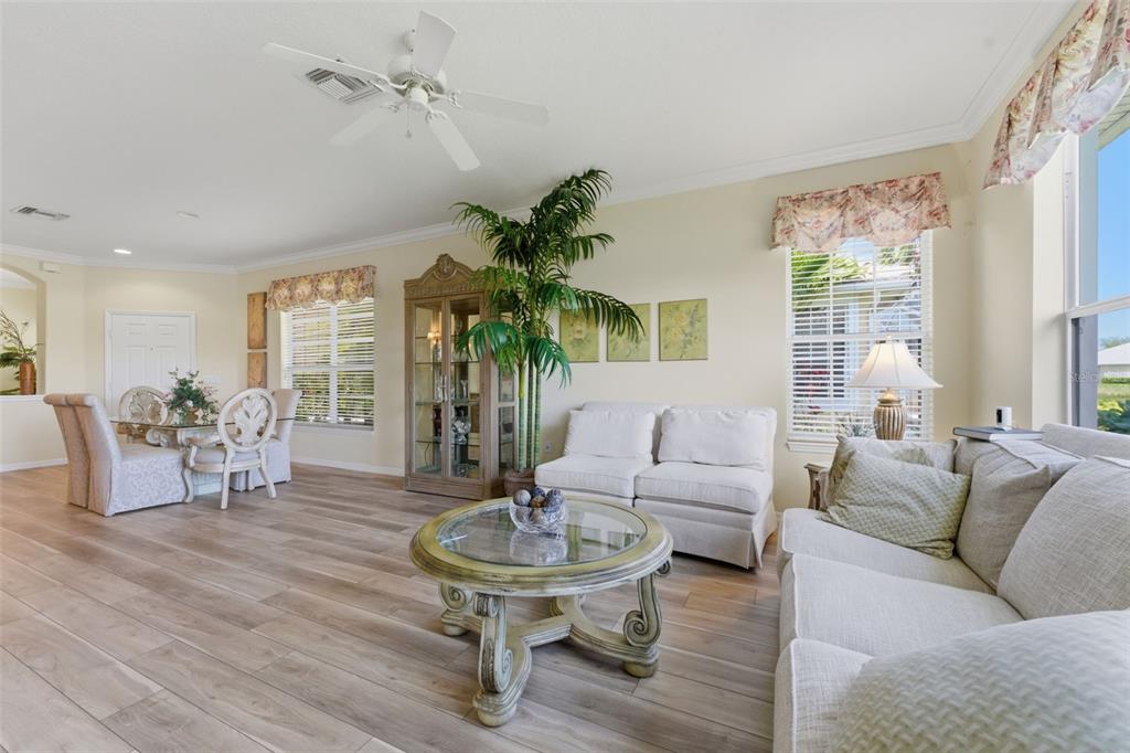 A living and dining area features light wood-look flooring, a ceiling fan, and neutral furniture — 4924 WHISPERING OAKS DRIVE, NORTH PORT, FL