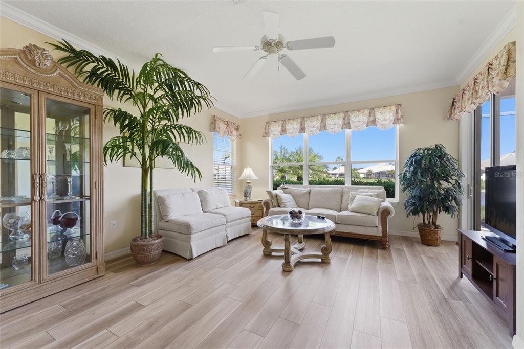 A living room features light wood-look flooring, two sofas, a glass coffee table, and plants — 4924 WHISPERING OAKS DRIVE, NORTH PORT, FL