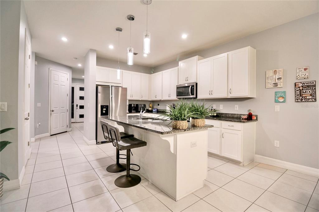 A kitchen features white cabinets, granite countertops, a center island with bar stools, and tile flooring — 2280 AVIAN LOOP, KISSIMMEE, FL