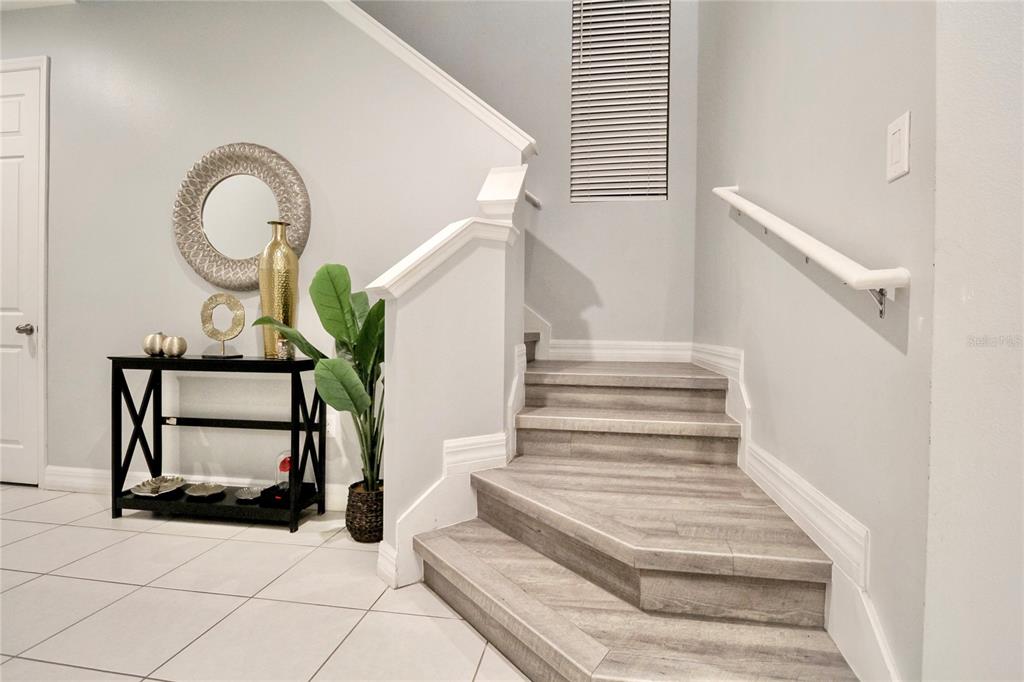 A staircase with wood-look steps sits beside a black console table and a potted plant — 2280 AVIAN LOOP, KISSIMMEE, FL