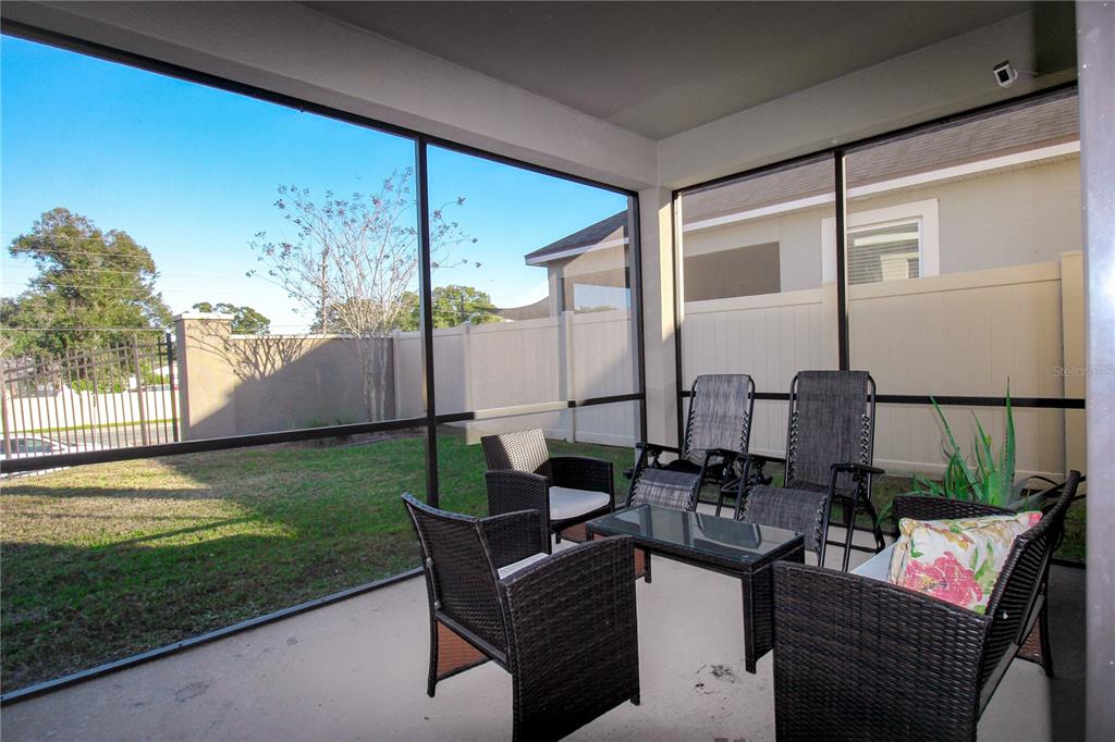 A screened-in patio features wicker furniture and a view of a fenced backyard — 2280 AVIAN LOOP, KISSIMMEE, FL