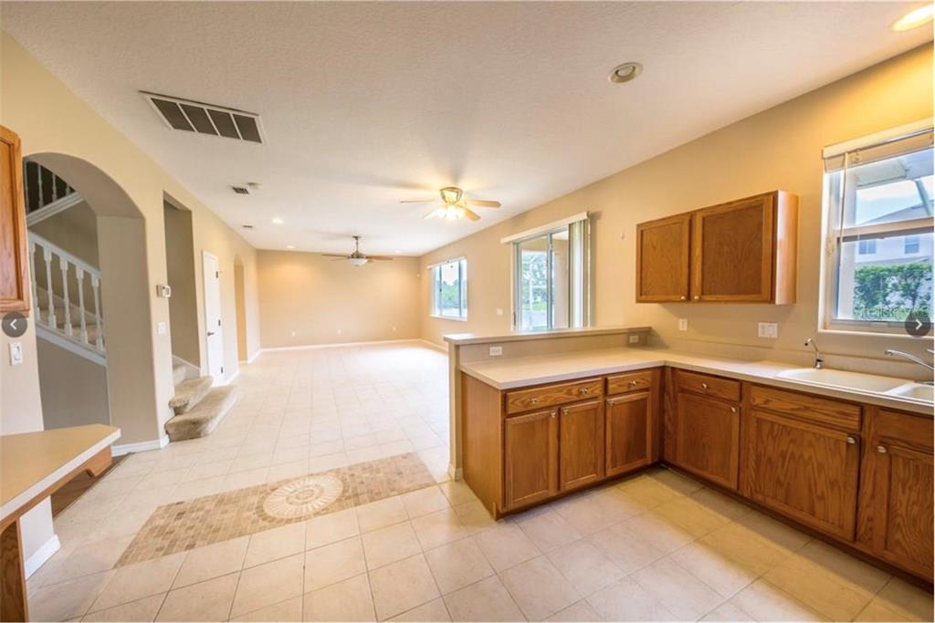 A kitchen with wood cabinets overlooks an open-concept living area with tile flooring — 6006 BROAD RIVER RUN, ELLENTON, FL