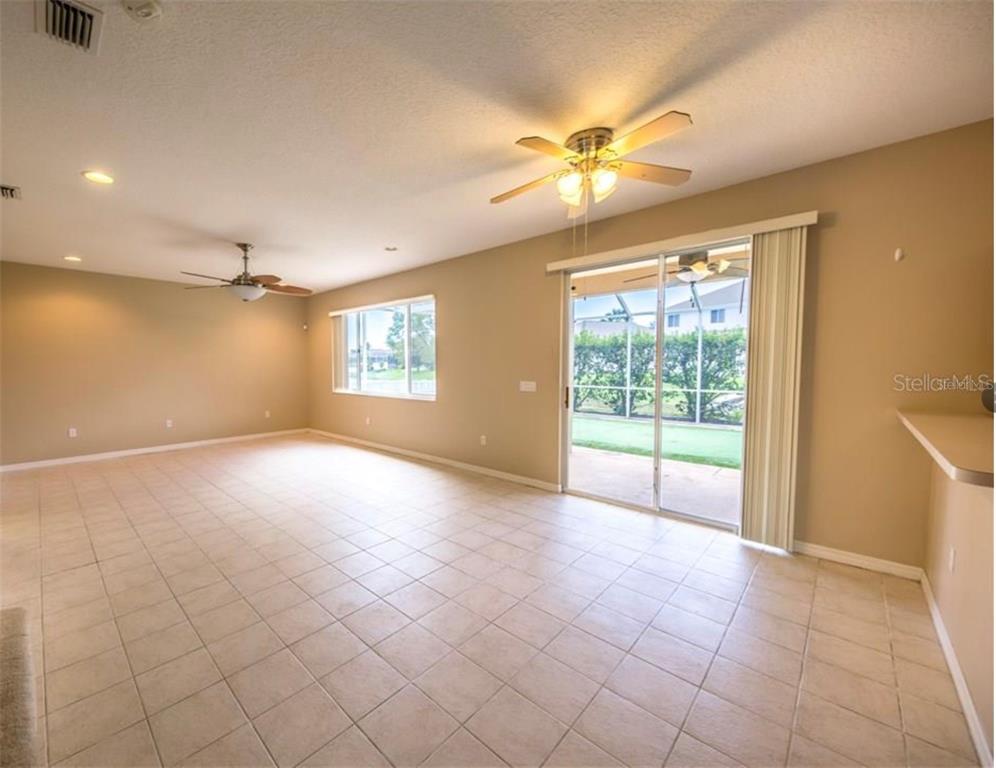 A spacious living room with beige walls, tile flooring, two ceiling fans, and sliding glass doors — 6006 BROAD RIVER RUN, ELLENTON, FL