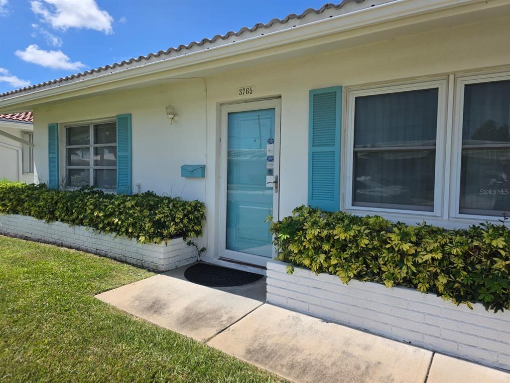 The exterior of a single-story house features a light-blue front door, shutters, and brick planters — 3765 101ST AVENUE N UNIT -, PINELLAS PARK, FL