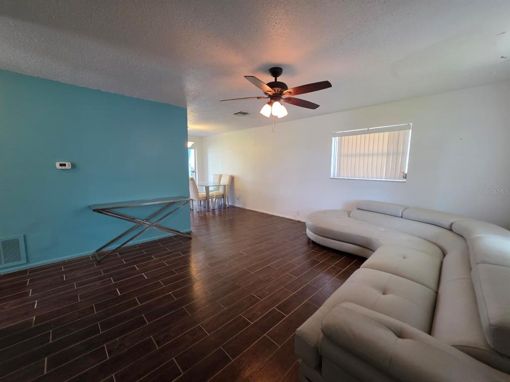 A living room features a white sectional sofa, wood-look tile floors, and a ceiling fan — 3765 101ST AVENUE N UNIT -, PINELLAS PARK, FL