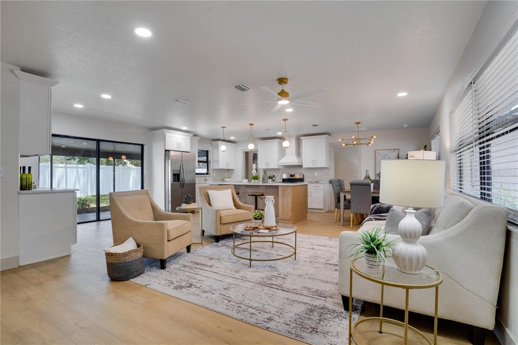 An open-concept living room and kitchen feature light wood flooring, white cabinetry, and neutral furniture — 2239 68TH AVENUE N, ST PETERSBURG, FL