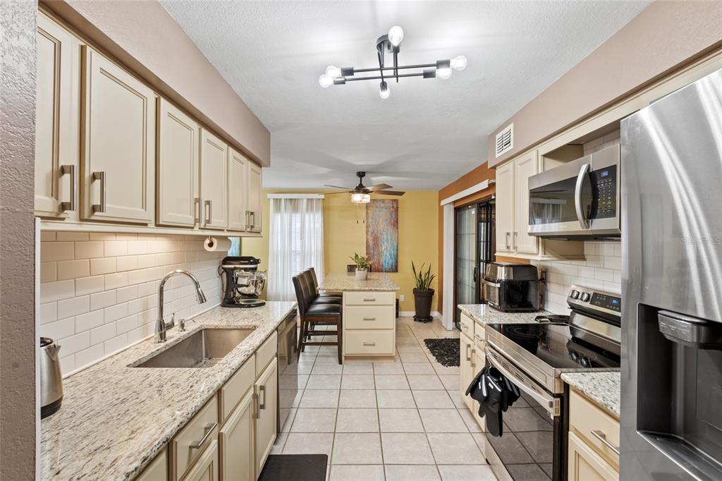 A kitchen features beige cabinets, granite countertops, stainless steel appliances, and a central dining island — 100 E OAK TERRACE DRIVE UNIT A2, LEESBURG, FL