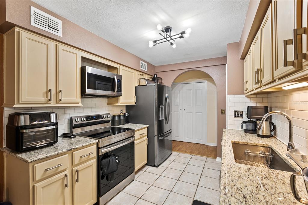 A kitchen features beige cabinets, granite countertops, stainless steel appliances, and white tile flooring — 100 E OAK TERRACE DRIVE UNIT A2, LEESBURG, FL