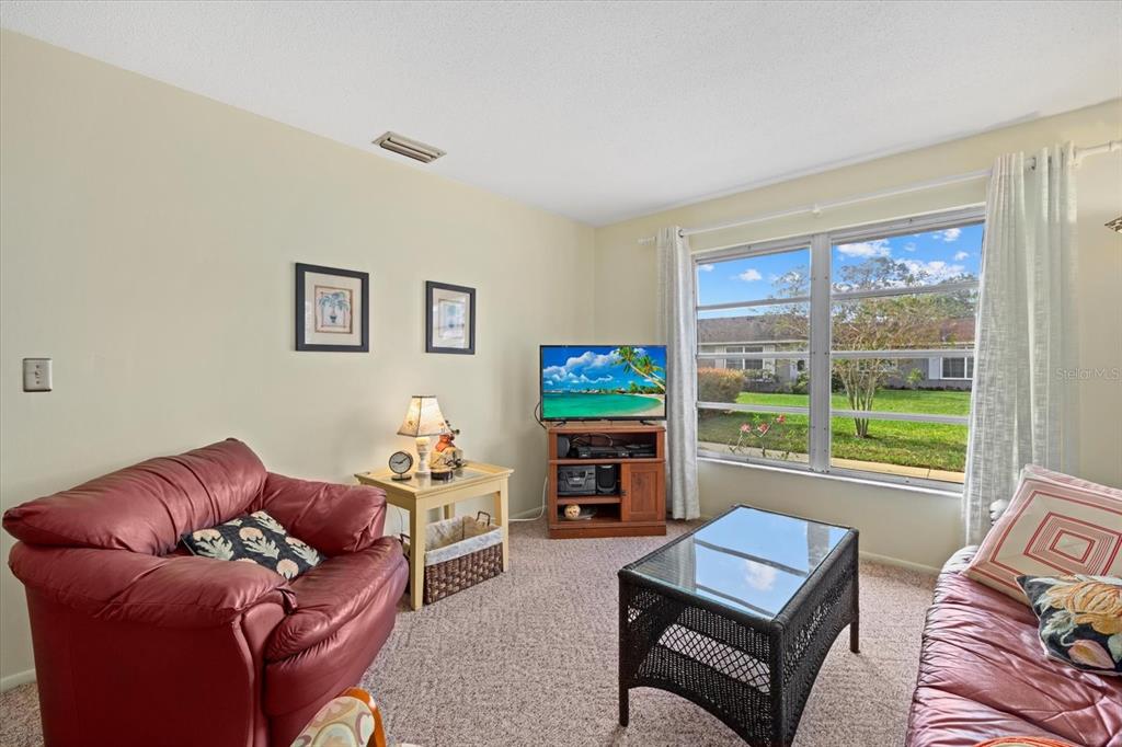 A living room features a red leather sofa, a glass-topped coffee table, and a television — 1343 GLENDALE CIRCLE W UNIT 216, SARASOTA, FL