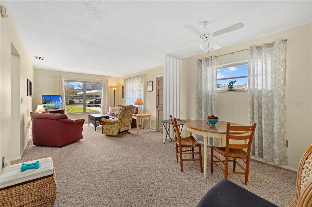 A living and dining area with beige carpet, a ceiling fan, and large windows — 1343 GLENDALE CIRCLE W UNIT 216, SARASOTA, FL