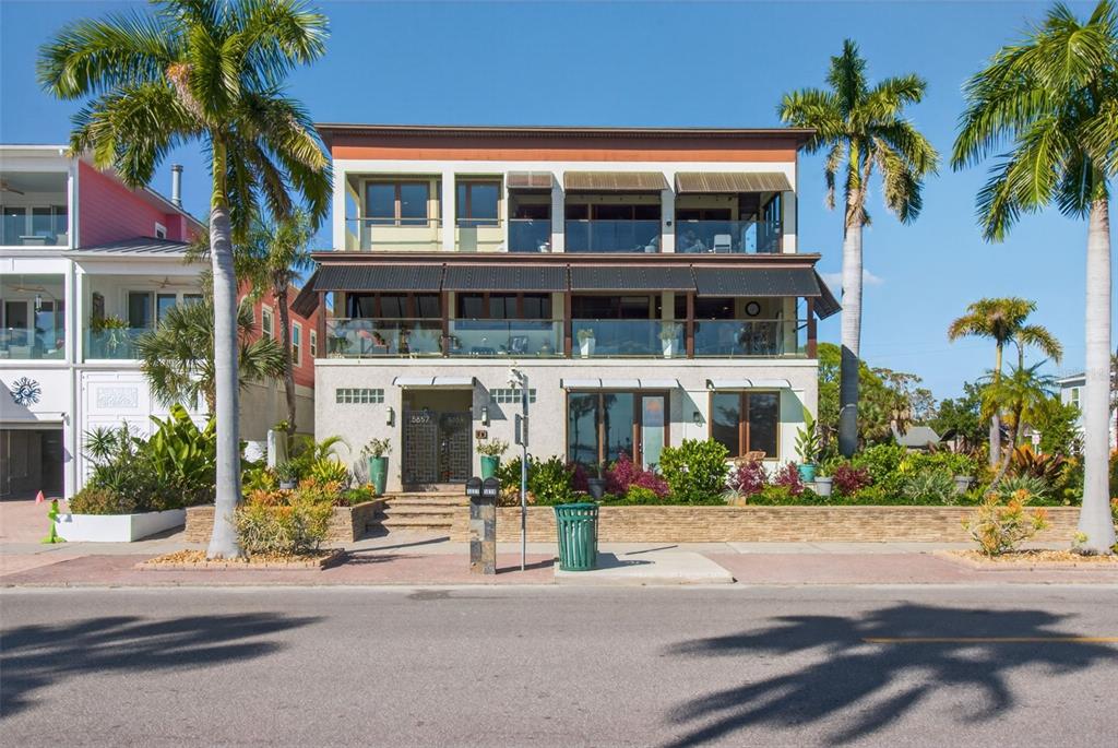 A three-story coastal home with balconies, large windows, and palm trees in the front yard — 5659 SHORE BOULEVARD S, GULFPORT, FL