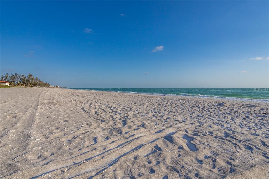 A wide, sandy beach stretches along the ocean under a clear blue sky — 560 GULF BAY ROAD, LONGBOAT KEY, FL
