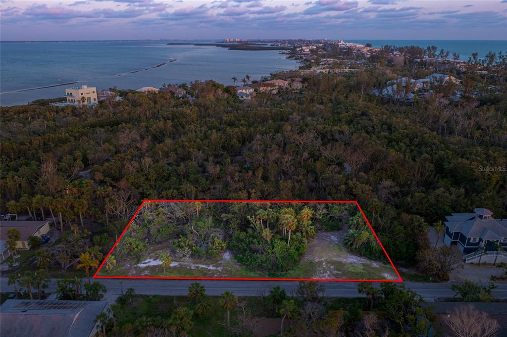 An aerial view shows a vacant, rectangular lot outlined in red along a coastal road — 560 GULF BAY ROAD, LONGBOAT KEY, FL