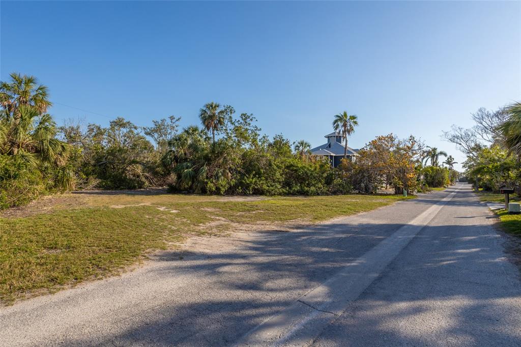 A vacant, grassy lot sits beside a paved road with dense trees and a house nearby — 560 GULF BAY ROAD, LONGBOAT KEY, FL