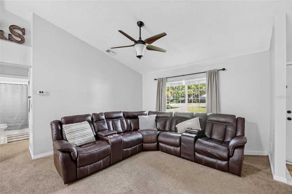 A living room features a large brown leather sectional sofa, beige carpet, and a ceiling fan — 11625 SE 53RD COURT, BELLEVIEW, FL