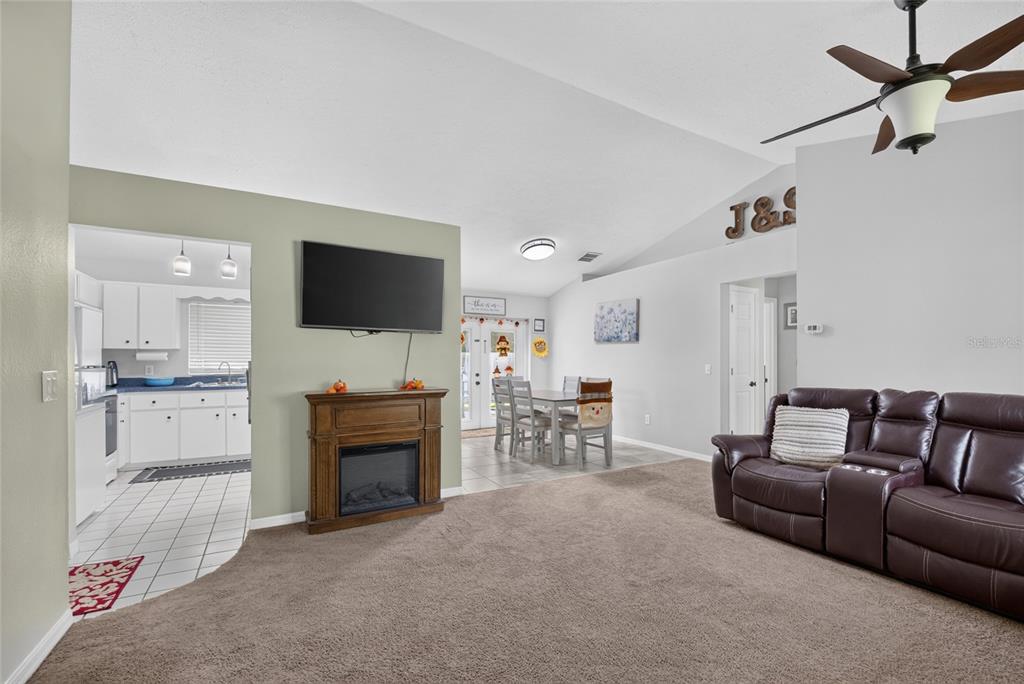A living room with a fireplace, television, and brown leather sofa opens into a kitchen — 11625 SE 53RD COURT, BELLEVIEW, FL